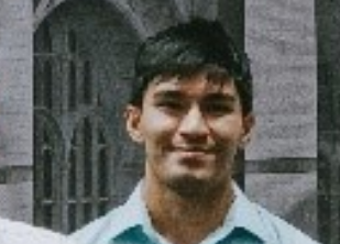 Photograph of a person with short black hair smiling, wearing a light blue shirt.